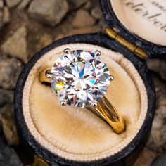 an engagement ring with a round brilliant diamond sits in a velvet box next to some rocks