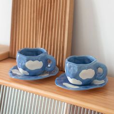 two blue cups and saucers sitting on top of a wooden shelf next to a radiator