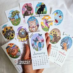 a hand holding a calendar with pictures of cats and flowers on it in front of a white sheet