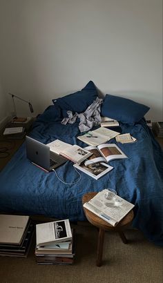 an unmade bed with many books on it and a laptop sitting on the end table