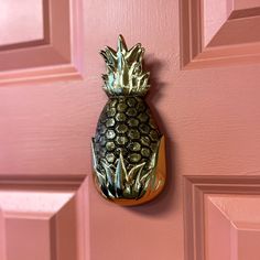 a metal pineapple hanging on the side of a pink door with gold foiling