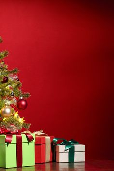 a small christmas tree with presents under it on a table next to a red wall