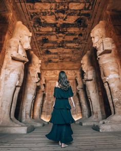 a woman in a black dress walking through an egyptian temple