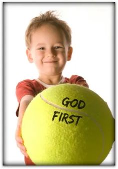 a young boy holding a tennis ball with the word god first written on it in black