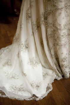 the back of a wedding dress with white and silver beading on it's skirt