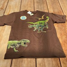 Size 10-12 Brand New Brown Dino Short Sleeve Graphic Tee Cute Brown Tops For Playwear, Casual Green Dinosaur Print Tops, Casual Green Tops With Dinosaur Print, Summer Dinosaur Print Short Sleeve Tops, Green Cotton Dinosaur Print Tops, Green Cotton Tops With Dinosaur Print, Brown Cotton Tops With Cartoon Print, Brown Cotton Top With Cartoon Print, Short Sleeve Dinosaur Print Tops For Playwear