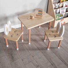 two children's wooden chairs and table with faces drawn on them in front of a bookshelf