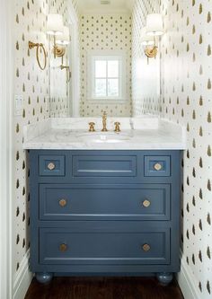 a bathroom vanity with blue drawers and white counter top, gold accents on the wall