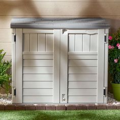 a white storage shed sitting next to a flower pot on top of a green lawn