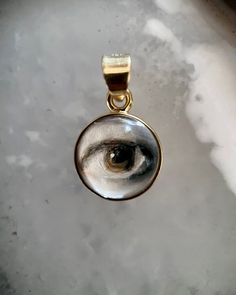 Lover's Eye pendant with an oil painting encased in gold plate over sterling with a quartz crystal cabochon which gives a magical magnifying effect, measuring 1/2" in diameter; 18" 16k gold over brass chain included. THE HISTORY: Lover's Eyes were a jewelry trend c.1785-1830 of brooches set with tiny watercolor portraits on ivory. Since they were cropped to eyes, they were in many ways more direct and intimate than traditional miniature portraits; but also because they were just eyes, they were Mystical Clear Jewelry For Gifts, Unique Gold Cabochon Jewelry, Unique Gold Jewelry With Cabochon, Artistic Gold Jewelry With Cabochon, Artistic Gold Necklace With Round Pendant, Spiritual Round Pendant Jewelry For Memorial, Spiritual Round Pendant Jewelry For Memorials, Spiritual Memorial Jewelry With Round Pendant, Artistic Bronze Round Jewelry