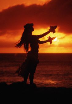 a woman standing on top of a beach next to the ocean holding a bird in her hand