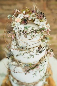 a tall white cake with flowers on it's sides and greenery around the edges