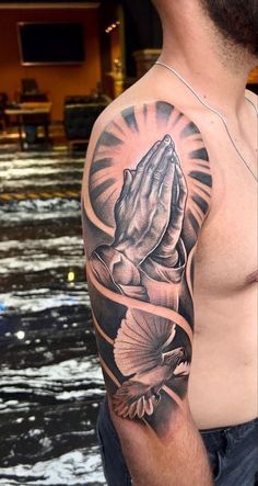 a man with a tattoo on his arm and chest holding a praying hand in front of him