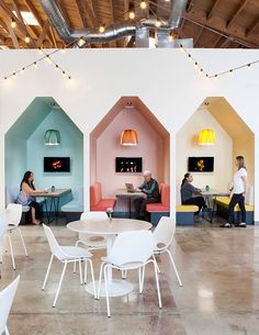 people are sitting at tables and chairs in an open space with exposed ceilings, white walls, and bright colored lighting