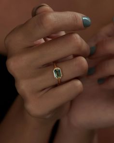 a woman's hand holding a ring with an emerald colored stone in the middle