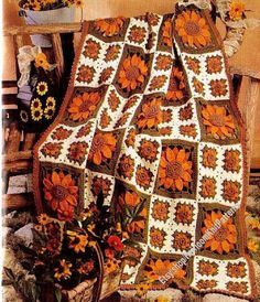 an orange and white crocheted blanket sitting on top of a wooden bench next to flowers