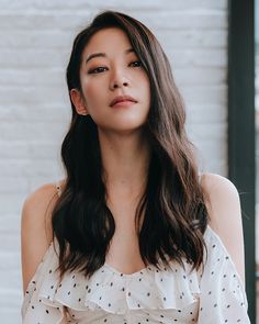 a woman with long dark hair wearing a white top and looking off to the side