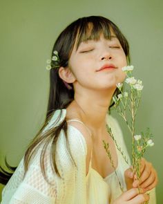 a woman holding flowers in her hands and looking up at the sky with eyes closed