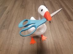 a toy duck holding a pair of scissors in it's beak on a wooden floor