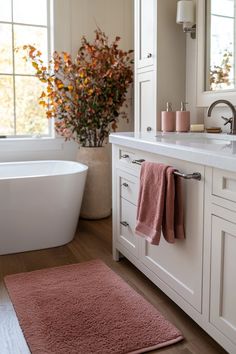 a white bath tub sitting next to a sink in a bathroom under a window covered with pink towels