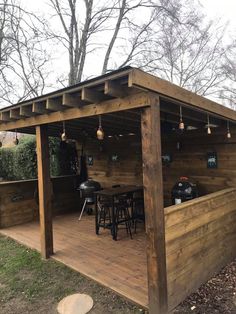 an outdoor bar with stools and tables under a wooden structure in the grass next to some trees