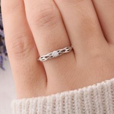 a woman's hand with a white gold ring on it and purple flowers in the background