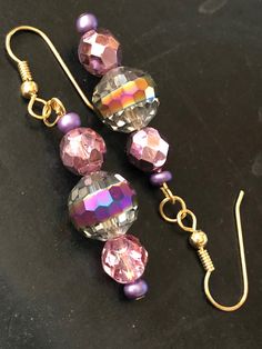 A lovely metallic drop earrings with loads of sparkle to dress up any holiday outfit. A fire polished central bead exhibits a purple tone which blends nicely with the faceted purple metallic beads on each side. The ear wire is nickel-free gold plate. Gold Beaded Earrings With Faceted Beads For Party, Gold Party Beaded Earrings With Faceted Beads, Party Gold Beaded Earrings With Faceted Beads, Party Beaded Drop Earrings With Ear Wire, Handmade Iridescent Crystal Earrings For Party, Beaded Drop Earrings For Party, Party Crystal Dangle Earrings With Ear Wire, Party Drop Earrings With Faceted Beads, Gold Crystal Earrings With Faceted Beads