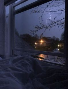 a bedroom with a window that has a view of the street outside and lightning in the sky