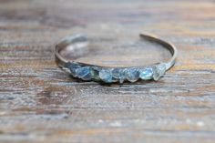 "Gemstone open gold or silver bangle with pieces of light gray Labradorite with flashes of blue and green. The setting is on a long rectangle that is 2\" long and a little under 1/4\" narrow, it is petite and slim. The cuff is gold or silver plated stainless steel and adjustable, 2\" x 2 1/2\" circumference.  The bracelet is made with natural stone each one has slight variations in size and shape. Your bracelet will be unique." Unique Labradorite Bangle Jewelry, Handmade Labradorite Bangle Jewelry, Labradorite Bracelet Jewelry Gift, Blue Labradorite Bracelet, Spiritual Labradorite Bracelet, Unique Moonstone Bangle Jewelry, Silver Labradorite Bangle Bracelets, Silver Labradorite Bangle Bracelet, Silver Bangle Cuff Bracelet With Natural Stones