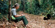 a man sitting in the middle of a forest looking at his cell phone and writing