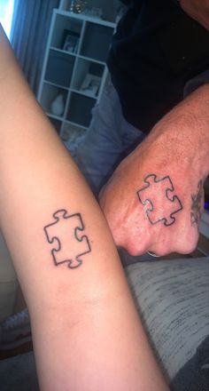 two people with matching tattoos on their arms holding each other's hands and one has a puzzle piece tattooed on the arm