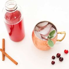 a copper mug filled with ice and cranberry tea next to cinnamon sticks on a white surface