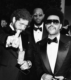 three men in tuxedos posing for the camera with one pointing at his finger