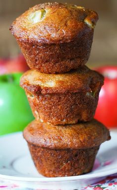 three muffins stacked on top of each other on a plate with apples in the background