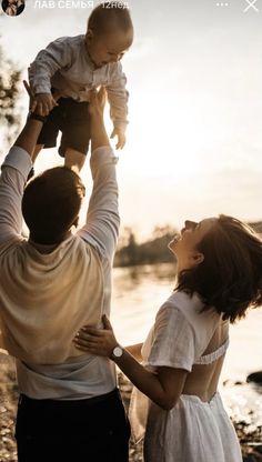 a man holding a baby up in the air while standing next to two other people