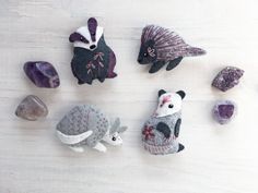 four small stuffed animals sitting next to each other on a white surface with rocks and stones around them