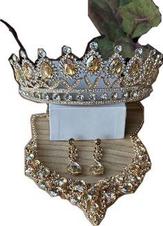 a crown, earrings and brooch sitting on top of a wooden stand next to a flower