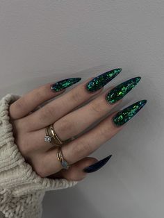 Daring and dynamic, these nails seem to have been dipped in the cosmic dust of a nebula. The stiletto shape serves as a canvas for the deep, enigmatic green, sprinkled with flecks of iridescent glitter that mimic the twinkling stars of the night sky. This nail idea is for those who aren't afraid to stand out and embrace their inner starlight. It's a bold statement that pairs well with the confidence of someone who knows they're meant to shine. Goth Nails, Gel Nails Diy, Vibrant Nails, Jelly Nails, Trendy Nail Design, Hot Nails, Dope Nails, Nail Polishes, Rhinestone Nails