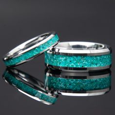 two wedding bands with turquoise glitter inlays are shown against a black background,