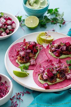 three tacos on a plate with lime wedges and red cabbage salad in the background