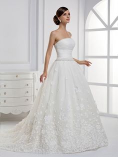 a woman in a white wedding dress standing next to a dresser with drawers on it