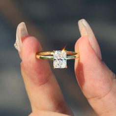 a woman's hand holding an engagement ring with a diamond in the middle and a yellow band around it