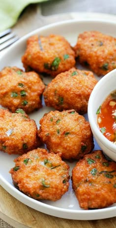 a white plate topped with fried food next to a bowl of sauce