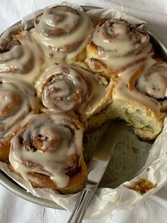 a pan filled with cinnamon rolls on top of a white table cloth next to a fork