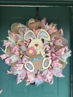 a pink and green wreath with a teddy bear on it's face, hanging from the front door