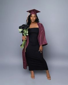 a woman wearing a graduation gown and holding flowers in her hand while standing against a gray background