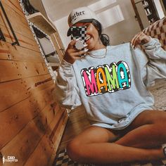 a woman sitting on the floor taking a selfie with her camera and wearing a sweatshirt that says mama