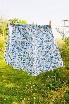 a blue and white flowered cloth hanging on a clothes line in the grass near some flowers