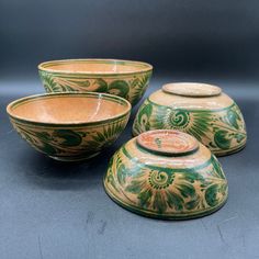 three green and yellow bowls with lids on grey table top, one has a flower design