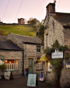 an old stone building with many windows and signs on the side of it in front of a grassy hill